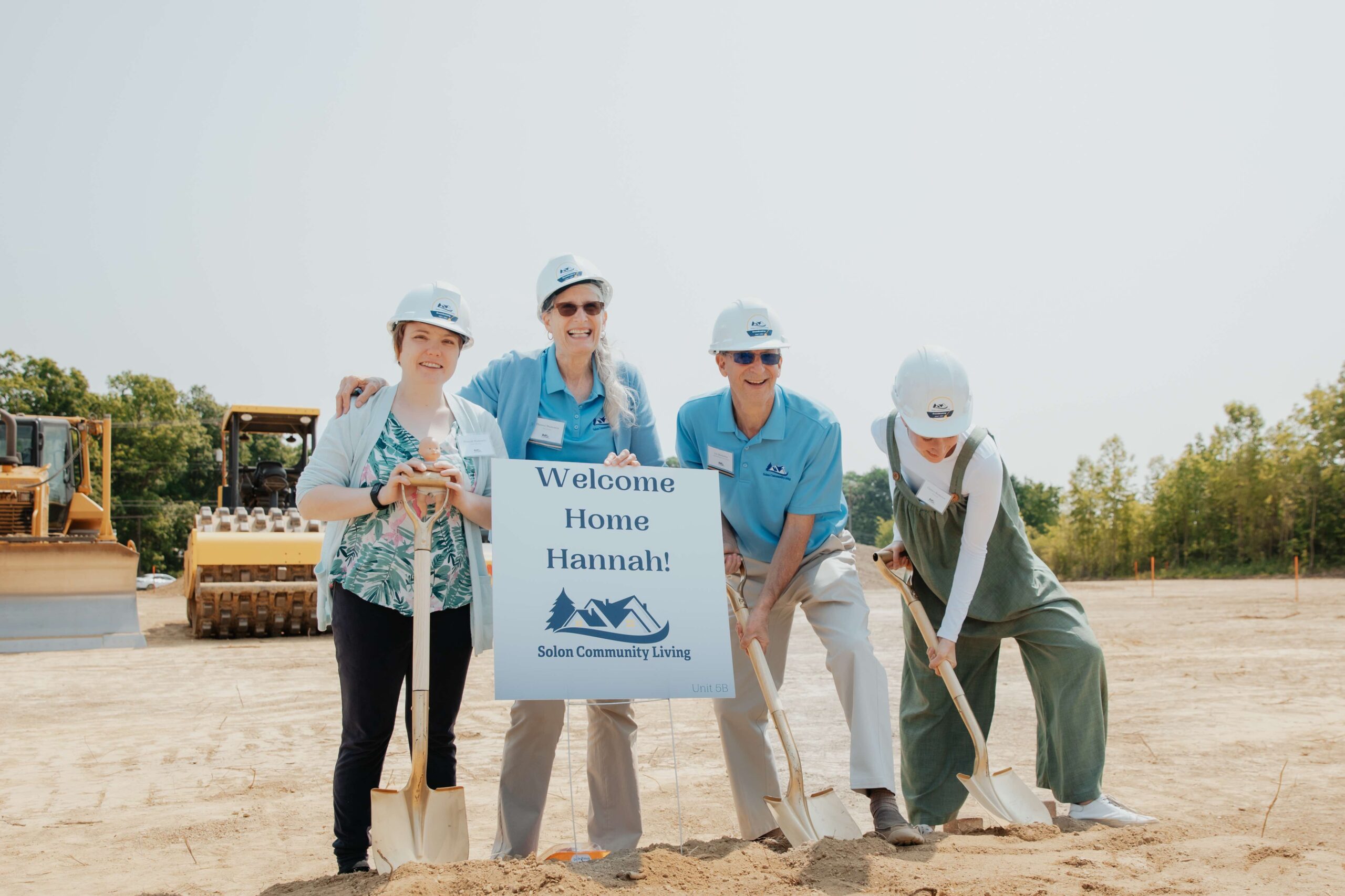 Family in front of welcome home sign digging into the dirt prior to beginning building.